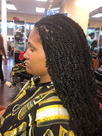 a woman is sitting in a salon with her hair braided