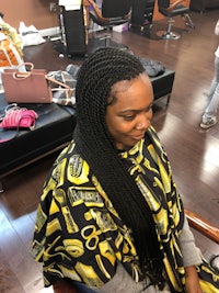 a woman sitting in a salon with braids on her head